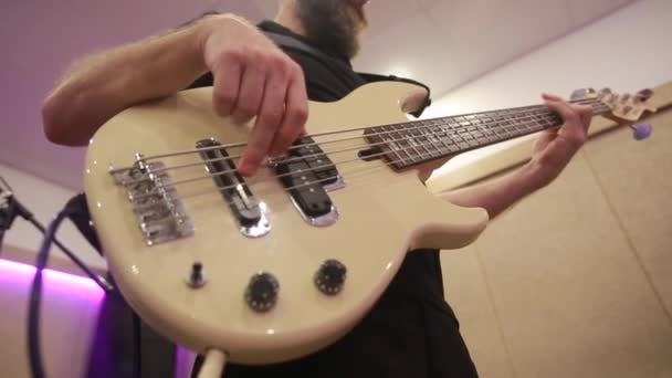 Close-up van mannelijke baardbassist handen spelen op elektrische basgitaar aanraken snaren op de repetitie — Stockvideo