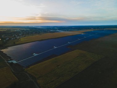 Parlak günbatımında kırsal alandaki büyük bir güneş çiftliğindeki büyük güneş panellerine hava aracı görüntüsü. Güneş pili santralleri, renkli fotoğraf