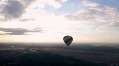 Avrupa 'nın küçük bir şehrindeki yeşil parkın üzerinde uçan renkli hava balonlarının hava aracı görüntüsü yaz günbatımında mavi bulutlu gökyüzünde