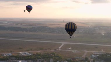 Yaz günbatımında bulutlu mavi gökyüzünde yeşil parkın ve nehrin üzerinde uçan renkli sıcak hava balonlarının insansız hava aracı görüntüsü