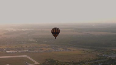 Renkli sıcak hava balonu, yaz günbatımında küçük bir Avrupa şehrinin yakınında bulutlu mavi gökyüzünde, havadan 4k manzaralı bir yerde uçuyor.