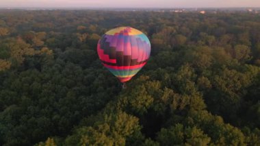Avrupa 'nın küçük bir şehrinde yaz gündoğumunda yeşil parkın ve nehrin üzerinde uçan renkli sıcak hava balonlarının insansız hava aracı görüntüsü