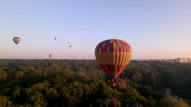 Avrupa 'nın küçük bir şehrinde yaz gündoğumunda yeşil parkın üzerinde uçan renkli sıcak hava balonları, hava manzarası