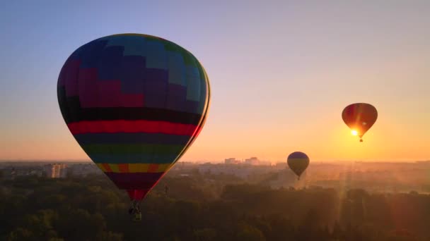 夏の日の出に緑の公園やヨーロッパの小さな都市の川を飛んでカラフルな熱気球の空中ドローンビュー — ストック動画