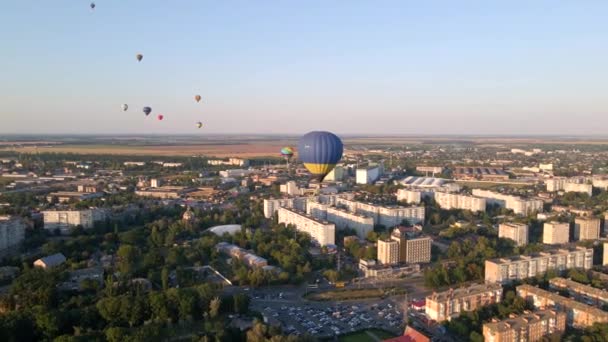 Luchtfoto drone uitzicht op kleurrijke hete lucht ballonnen vliegen over groen park en industriële wijk in kleine Europese stad bij zonsondergang — Stockvideo