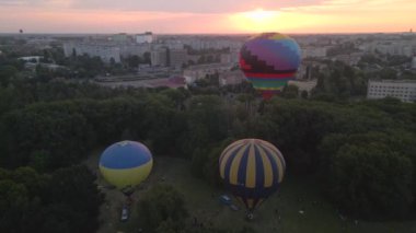 Avrupa 'nın küçük bir şehrinde yaz gündoğumunda yeşil parkın üzerinde uçan renkli sıcak hava balonunun insansız hava aracı görüntüsü