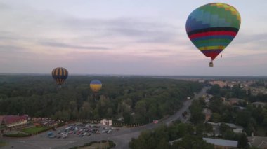 Avrupa 'nın küçük bir şehrinde yaz gündoğumunda yeşil parkın üzerinde uçan renkli sıcak hava balonları, hava manzarası