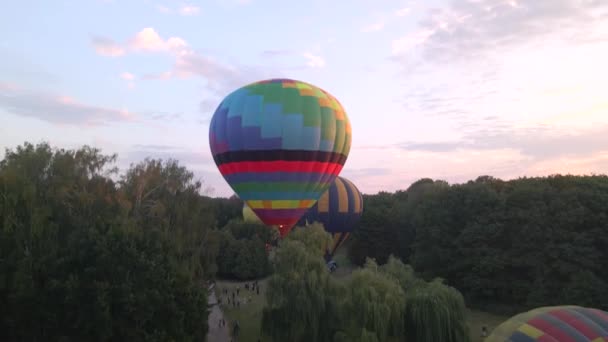 Luchtfoto drone uitzicht op kleurrijke hete lucht ballon vliegen over groen park in kleine Europese stad bij zonsopgang — Stockvideo