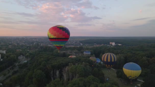 Barevné horkovzdušné balónky létající nad zeleným parkem v malém evropském městě za letního východu slunce, letecký pohled — Stock video