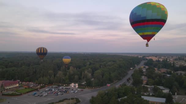 Colorful hot air balloons flying over green park in small european city at summer sunrise, aerial view — Stock Video