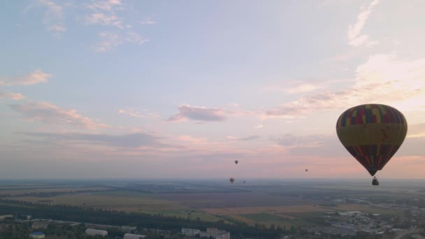 Kleurrijke hete lucht ballonnen vliegen over groen park en gebouwen in kleine Europese stad bij zonsopgang, luchtfoto 's — Stockvideo