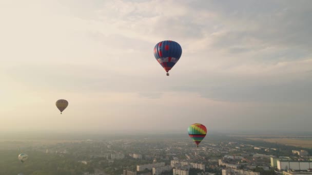 Барвисті повітряні кулі, що літають над будівлями в маленькому європейському місті на літній захід сонця, вигляд з повітря — стокове відео