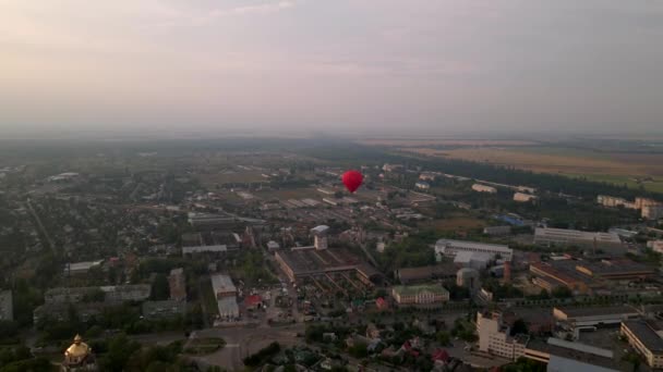 Красный воздушный шар, летящий над зданиями в индустриальной зоне в маленьком европейском городе на летнем закате, вид с воздуха — стоковое видео