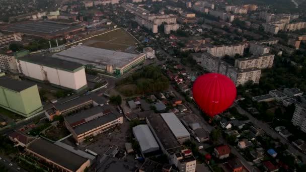Palloncino rosso che sorvola gli edifici nella zona industriale della piccola città europea al tramonto estivo, vista aerea — Video Stock