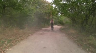 Genç sporcu kadının havadan çekilmiş yavaş çekimi yaz akşamları tozlu yolda bisiklet sürüyor. Sağlıklı bisiklet yaşam tarzı