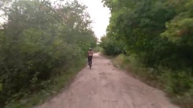 Genç spor kadının havadan çekilmiş fotoğrafı yaz akşamları tozlu kırsal yolda bisiklet sürüyor. Sağlıklı bisiklet yaşam tarzı