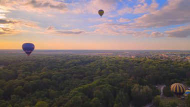 Ukrayna 'nın Kiev bölgesinde yaz gündoğumunda küçük Avrupa şehrinde yeşil park ve nehir üzerinde uçan renkli sıcak hava balonlarının insansız hava aracı görüntüsü
