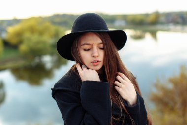 Bulanık arkaplanda siyah şapkalı, uzun saçlı güzel, modaya uygun bir kadının yakın plan portresi. Kadın modası, güzellik konsepti. Açık hava..