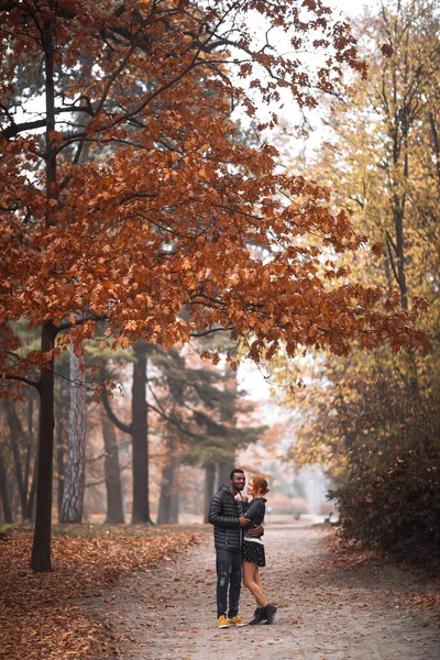 秋の公園を歩く幸せな異人種間のカップル 黒男と白の赤毛の女性 — ストック写真