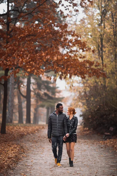 Happy interracial couple walking in autumn park, black man and white redhead woman