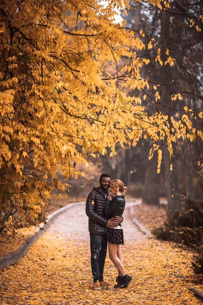 Sonbahar parkında yürüyen mutlu ırklar arası çift, siyah adam ve beyaz kadın.