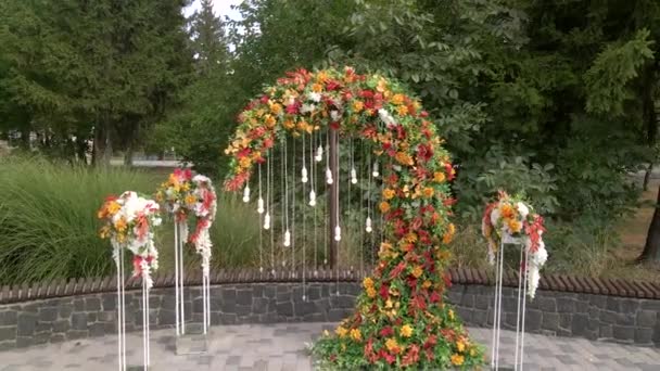 Cerimónia de casamento vista aérea com arco decorado com folhas e flores de outono, cadeiras brancas para os convidados, ao ar livre — Vídeo de Stock