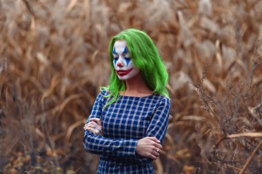 Portakal yapraklı sazlıklara Joker makyajlı yeşil saçlı bir kızın portresi..