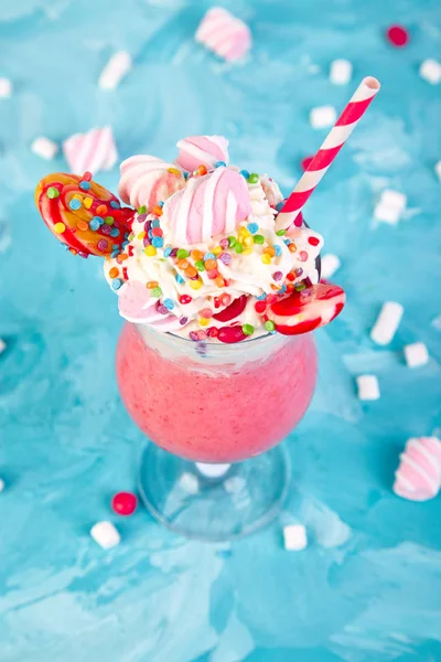 Pink Extreme milkshake with berry, rasberry, strawberry, candy marshmallow, lollipops on blue background.. Crazy freakshake. Copy space. Food trend Overshake