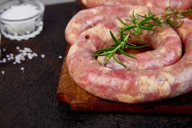 Biberiye, tuz ve peper ahşap kesme tahtası üzerinde ham sarmal domuz sosisi.