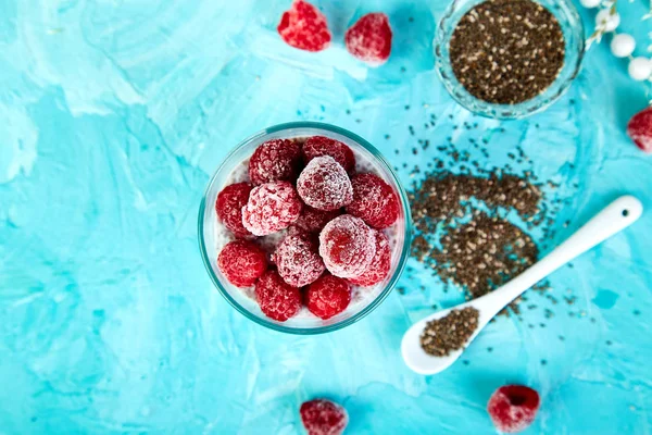 青い背景上にガラスにラズベリーと健全なチアのプリン ビーガン クリーミーな朝食 デトックスと健康的なスーパー フード朝食コンセプト — ストック写真