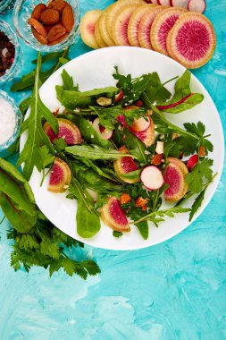 Madde karışımı yaprak turp, marul, mangold, maydanoz, roka, badem, çevresinde beyaz tabak salata tuz, lezzetli, balsamik, pepper. Sağlıklı diyet açık yiyecek Vegan düz kopya alanı yatıyordu 