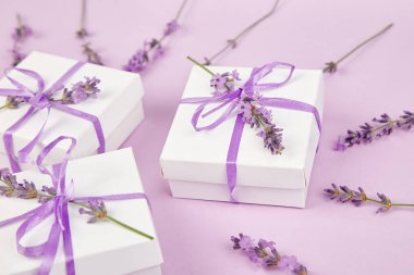 Mor Şerit ve buket çiçek lavanta pembe bir arka plan üzerinde beyaz hediye kutusu. Kutlama, Doğum günü. Dekorasyon mevcut. Düz yatıyordu. Kopya alanı.