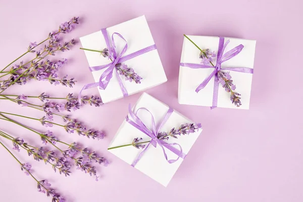Mor Şerit ve buket çiçek lavanta pembe bir arka plan üzerinde beyaz hediye kutusu. Kutlama, Doğum günü. Dekorasyon mevcut. Düz yatıyordu. Kopya alanı.