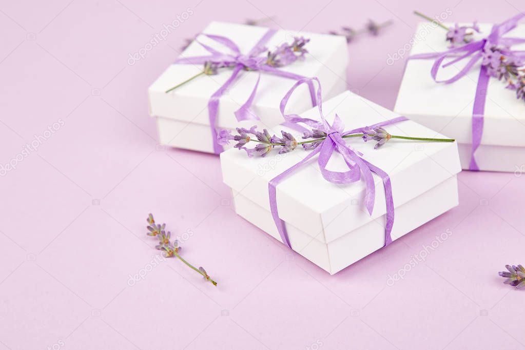 White Gift box with violet ribbon and bouquet of flower lavender on pink background. Celebration, birthday. Decoration present. Copy space.