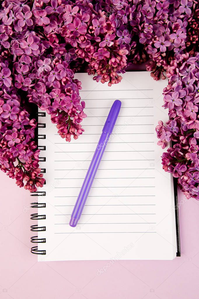 Branches of spring flowers bouquet blooming lilac on purple table. Woman diary notebook. Creative design of flowers. Flat lay. Place for text.