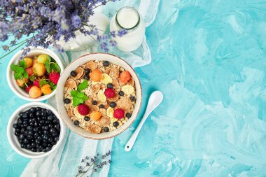 Sağlıklı vejetaryen kahvaltı. Yulaf ezmesi, granola ahududu ve yaban mersini kase üzerinde mavi arka plan, buket lavanta ile. Üstten görünüm. Düz yatıyordu. 