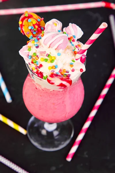 Pink Extreme milkshake with berry, rasberry, strawberry, candy marshmallow, lollipops on black background.. Crazy freakshake. Copy space. Food trend Overshake