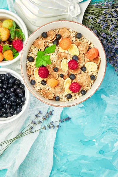 Healthy vegetarian breakfast. Oatmeal, granola with raspberries and blueberry in bowl over blue background, Bouquet lavender. Top view. Flat lay.