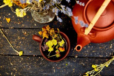 Bardak bitkisel çay - tutsan, adaçayı, kekik, helichrysum, lavanta yakınındaki koyu ahşap arka plan üzerinde kahverengi çaydanlık. Bitkisel çay. Kuru otlar ve çiçekler, bitkisel ilaç. Düz yatıyordu
