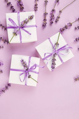 Mor Şerit ve buket çiçek lavanta pembe bir arka plan üzerinde beyaz hediye kutusu. Kutlama, Doğum günü. Dekorasyon mevcut. Düz yatıyordu. Kopya alanı.