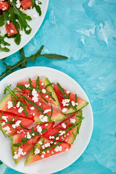 Taze yaz karpuz salatası beyaz peynir ve roka mavi masa arka plan üzerinde. Vegan gıda. Diyet, vejeteryan. Üstten görünüm. Düz yatıyordu. Kopya girintili