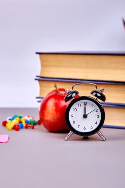 Okula dönüş sağlar. Kitap ve yeşil zemin üzerine kırmızı elma. Çalar saat ile natürmort. Kopya alanı.