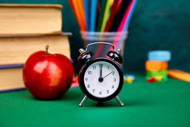Okula dönüş sağlar. Kitap ve yeşil zemin üzerine kırmızı elma. Çalar saat ile natürmort. Kopya alanı.