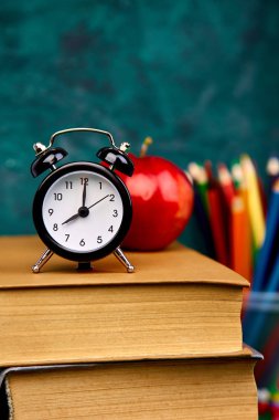 Okula dönüş sağlar. Kitap ve yeşil zemin üzerine kırmızı elma. Çalar saat ile natürmort. Kopya alanı.