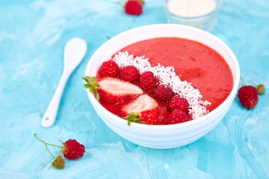 Güler yüzlü kase. Mavi arka plan üzerinde sağlıklı kahvaltı kase. Çilek ve Hindistan cevizi ile ahududu güler yüzlü. Vegan gıda