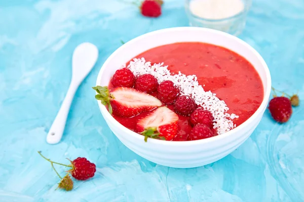 Güler yüzlü kase. Mavi arka plan üzerinde sağlıklı kahvaltı kase. Çilek ve Hindistan cevizi ile ahududu güler yüzlü. Vegan gıda