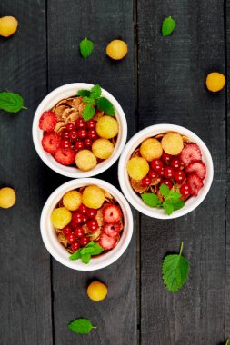 Sağlıklı kahvaltı beyaz kase üzerinde. Taze gevrek, müsli veya meyveler - sarı ahududu, akımlar ve siyah arka plan üzerine çilek ile tahıl. Diyet yemekleri. Açık yemek. Üstten görünüm. Uzay kopyalayın. Düz yatıyordu.