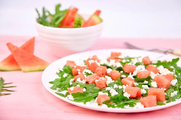 Fresh summer watermelon salad with feta cheese and arugula on pink table background. Vegan food. Diet, Vegetarian. Copy spac