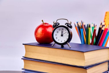 Okula dönüş sağlar. Kitap ve yeşil zemin üzerine kırmızı elma. Çalar saat ile natürmort. Kopya alanı.