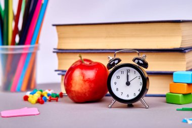 Okula dönüş sağlar. Kitap ve yeşil zemin üzerine kırmızı elma. Çalar saat ile natürmort. Kopya alanı.